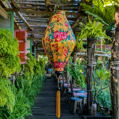 Tube shaped floral lantern hanging in a garden setting with greenery and wooden structures.