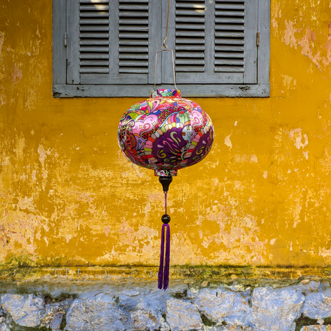 Round shaped lantern hanging in front of a vibrant yellow wall and grey shutters in Old Town with a print featuring colourful patterns and shapes.