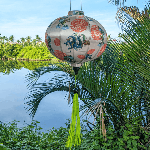 Round Vietnamese silk lantern with green tassel and print of green and blue dragons in the wild.