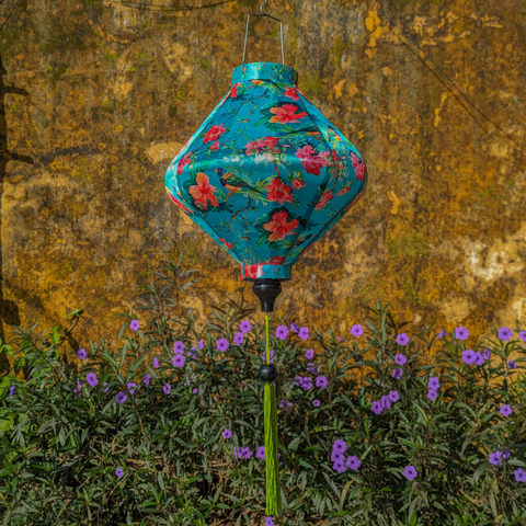 Lozenge shaped lantern hanging in Old Town, Hoi An with a yellow wall and purple flowers in the background.