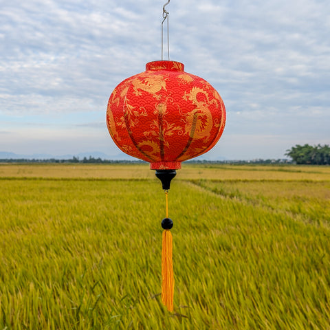 Orange lantern with gold patterns hanging over a rice field