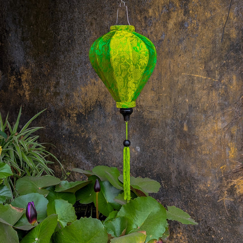 Green Jacquard silk Vietnamese lantern hanging in Old Town against an ancient wall and water fountain with black water lillies.