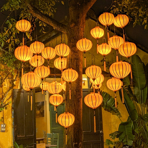 Vietnamese plain orange silk lanterns hanging in a tree creating a gorgeous yellow glow in Hoi An Old Town.