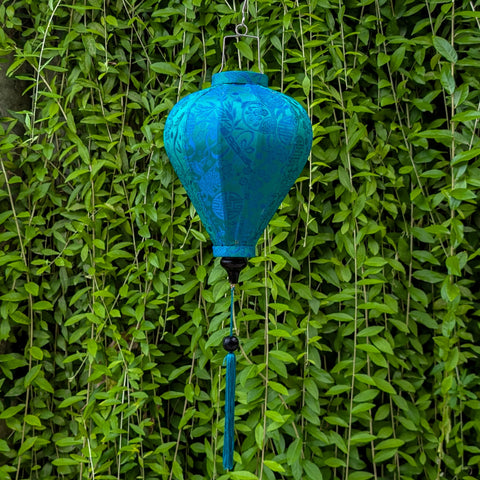Teal jacquard silk lantern hanging against a green leafy background