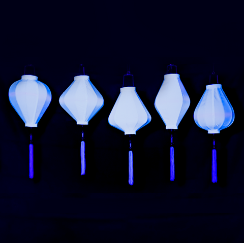 A row of glowing white silk lanterns in Balloon, Lozenge, Teardrop, Tube and Garlic shapes under  UV light.