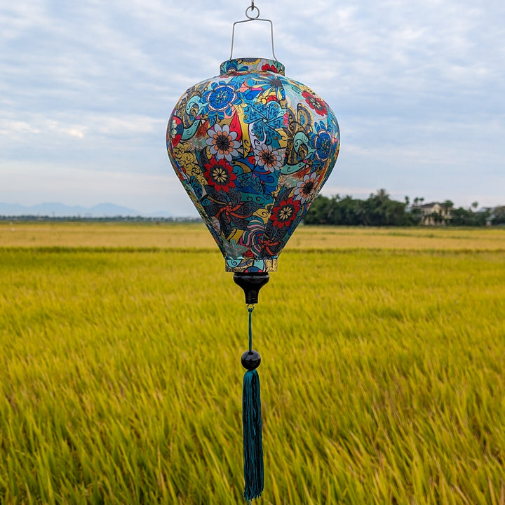 A balloon shape Vietnamese silk Hoi An lantern with an abstract print surrounded by yellow rice fields at harvest time.