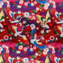 Polyester silk fabric with cranes, their wings gracefully cascading in shades of white, gold, red, and blue. Their backdrop is lush with red and pink flowers, foliage, and dark, majestic purples. 