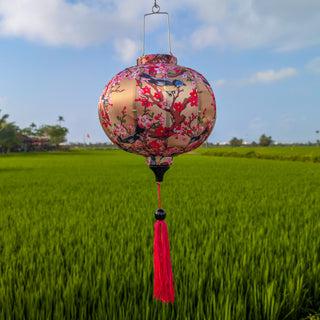 Round shaped lantern with floral and birds design hanging against a green field and blue sky.