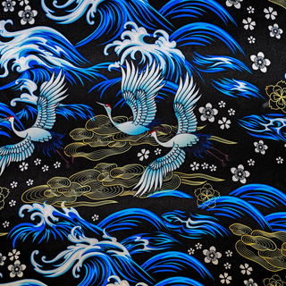 Close up of polyester silk fabric print of birds in graceful flight, set against a sleek black background adorned with rolling waves, floating flowers and intricate gold illustrations.