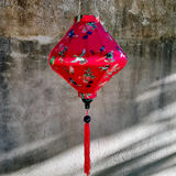 Lozenge shaped lantern against grey wall with a print of various birds in flight against a hot pink backdrop.