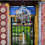 Lozenge shaped lantern hanging in front of a temple with different colour painted walls and cat in the background.