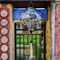 Lozenge shaped lantern hanging in front of a temple with different colour painted walls and cat in the background.