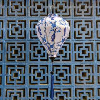 Balloon shaped lantern with dark blue floral patterns with dark blue tassel hanging against a geometric patterned wall.