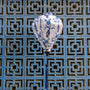 Balloon shaped lantern with dark blue floral patterns with dark blue tassel hanging against a geometric patterned wall.