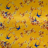 Polyester silk fabric with a print featuring blue swallows flying around with yellow flowers in their beaks on a yellow background.