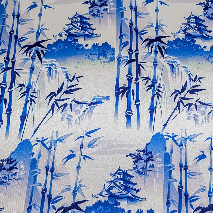 Polyester silk fabric featuring a blue print of temples and pagodas high above hilltops with large bamboo trees floating against white background. 