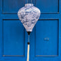 Balloon shape Vietnamese silk lantern with a illustration of bonsai trees in blue against white. Hanging in front of blue shutters in Hoi An.