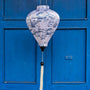 Balloon shape Vietnamese silk lantern with a illustration of bonsai trees in blue against white. Hanging in front of blue shutters in Hoi An.