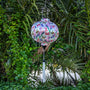 Cream silk lantern with butterfly pattern hanging among green foliage on a river.