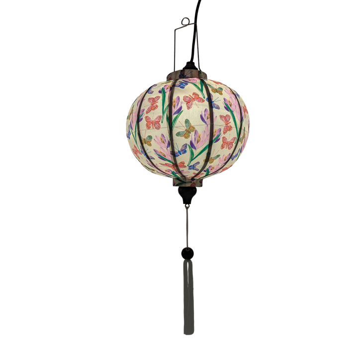Glowing Round shaped lantern with white tassel made with bamboo, steel and a print of stunning print of blue, red and green butterflies fluttering around pink and purple flowers.