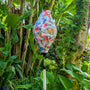 Tube shape lantern with butterfly pattern and white tassel hanging among green foliage
