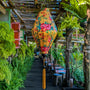 Tube shaped floral lantern hanging in a garden setting with greenery and wooden structures.
