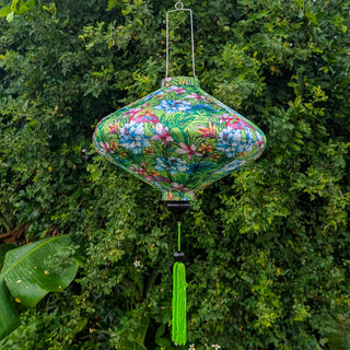 UFO shaped silk lantern with tropical pattern of chameleons, flamingos and hibiscus flowers hanging against a green leafy background
