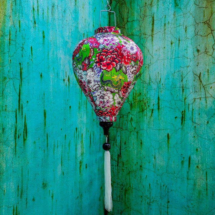 A balloon shaped Vietnamese lantern with little green dragons and Chrysanthemums on a vibrant lime green background shot against a textured blue and green wall.