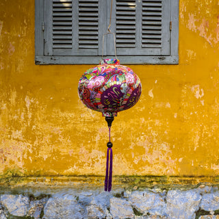 Round shaped lantern hanging in front of a vibrant yellow wall and grey shutters in Old Town with a print featuring colourful patterns and shapes.