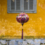 Round shaped lantern hanging in front of a vibrant yellow wall and grey shutters in Old Town with a print featuring colourful patterns and shapes.
