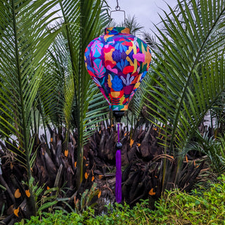 Balloon shaped lantern with purple tassel hanging outside in front of palm trees on a river.