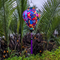 Balloon shaped lantern with purple tassel hanging outside in front of palm trees on a river.