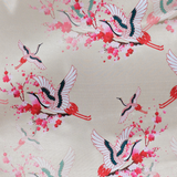 Up close polyester silk fabric featuring majestic cranes in vivid reds, hints of teal and delicate blossoms against a calming creamy backdrop. 