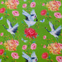 A vibrant fabric design featuring a green background with elegant white cranes in flight, their wings gracefully spread with black and blue accents. Surrounding them are lush chrysanthemums in shades of red, pink, and yellow, along with delicate roses, small blue butterflies and dragonflies.
