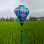 A vibrant blue Hoi An silk lantern featuring elegant white cranes, lush green lotus leaves, and striking pink lotus flowers. The intricate hand-painted design adds a touch of nature and tradition, while the matching blue tassel enhances its graceful aesthetic. Set against a backdrop of lush green rice fields, this lantern beautifully represents Vietnamese craftsmanship and cultural artistry.