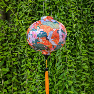 Round lantern with flowers, geometric shapes and bird design on orange against a green leafy background
