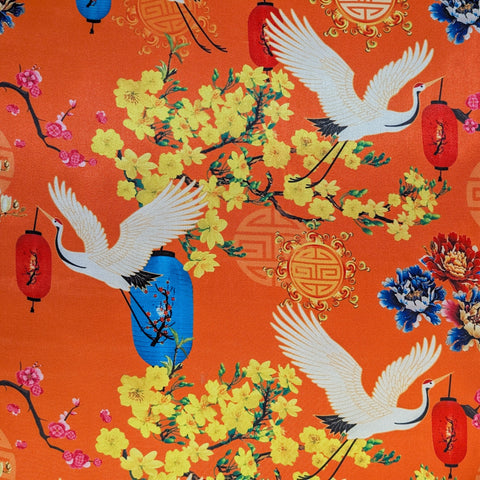 Decorative fabric with cranes, flowers, and lanterns on an orange background
