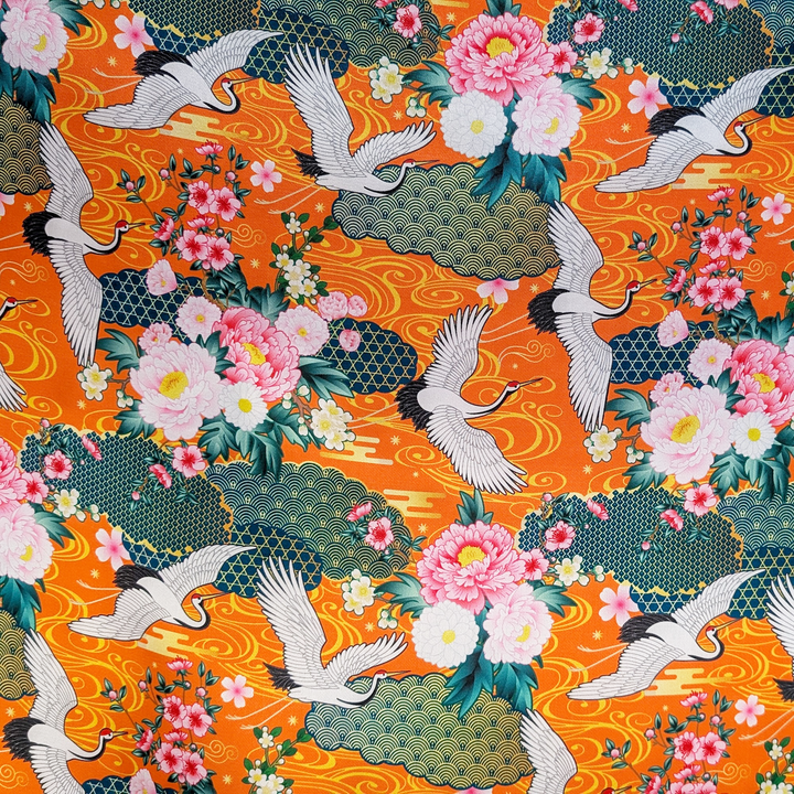 Print of white cranes and pink flowers with geometric patterns in teal and gold colours against an orange background