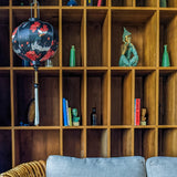 Round shape Vietnamese lantern hanging in front of a shelf featuring white cranes and orange flowers on black backdrop.