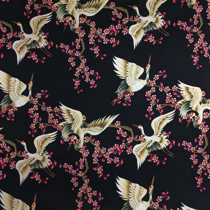 Polyester silk fabric with red-headed white cranes amongst pink cherry blossoms against a black background.