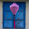 Balloon shaped Vietnamese Hoi An lantern with a pink tassel hanging in front of blue shutters.