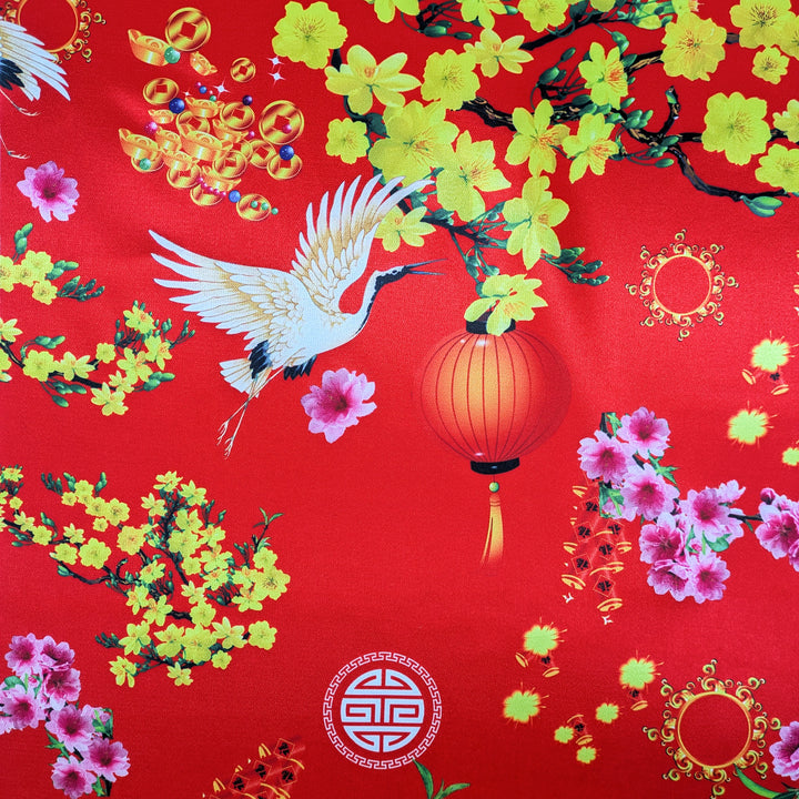 Close up of polyester silk fabric with a print featuring red headed cranes in flight, yellow and pink flowers, symbolism and orange lanterns against red background.