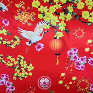 Close up of polyester silk fabric with a print featuring red headed cranes in flight, yellow and pink flowers, symbolism and orange lanterns against red background.