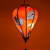 Balloon shape lantern glowing with a red hue with white red-headed cranes, gold and blue flowers on a red silk fabric.