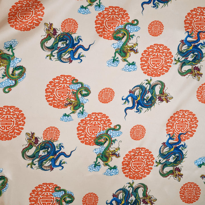 Polyester silk fabric with green and blue dragons on a rich creamy backdrop.