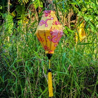 Tube shaped lantern hanging outside with a print of Red and white dragons on yellow background.