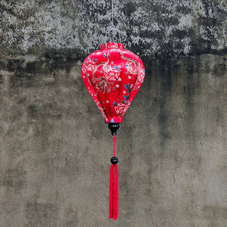 Balloon shaped Vietnamese Hoi An Lantern with red tassel and print of golden dragons and large pink chrysanthemums hanging in front of a grey wall.