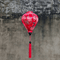 Balloon shaped Vietnamese Hoi An Lantern with red tassel and print of golden dragons and large pink chrysanthemums hanging in front of a grey wall.