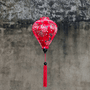 Balloon shaped Vietnamese Hoi An Lantern with red tassel and print of golden dragons and large pink chrysanthemums hanging in front of a grey wall.