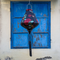 Teardrop shaped lantern with green and blue dragons on a black backdrop and tassel hanging in front of a blue window.